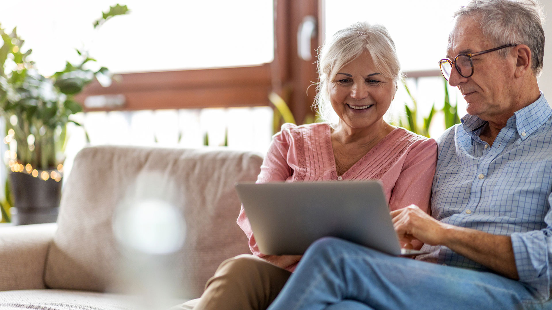 Two people sit on a couch and look at a laptop.