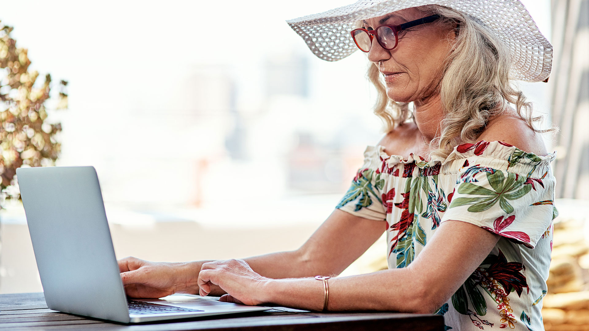 A person sits at an outdoor table and looks at a laptop.