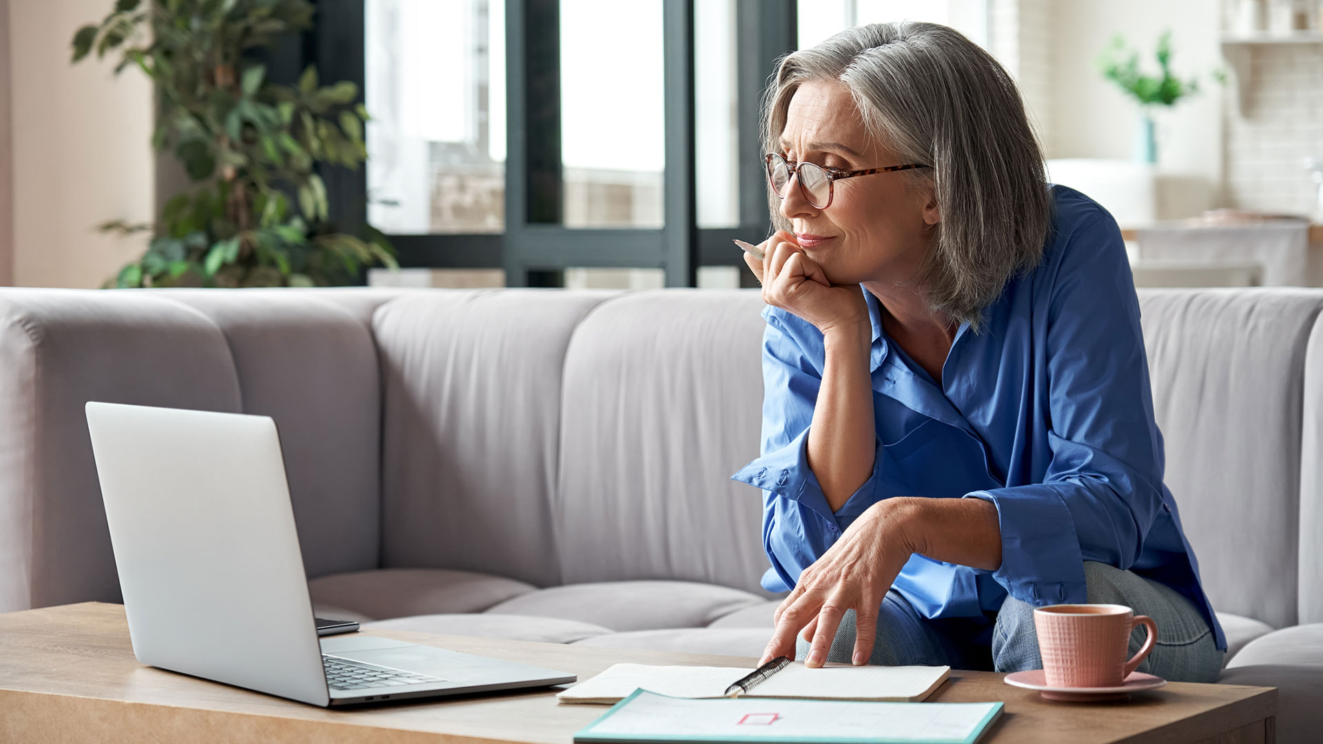 A person sits on a couch and looks at a laptop on a coffee table.