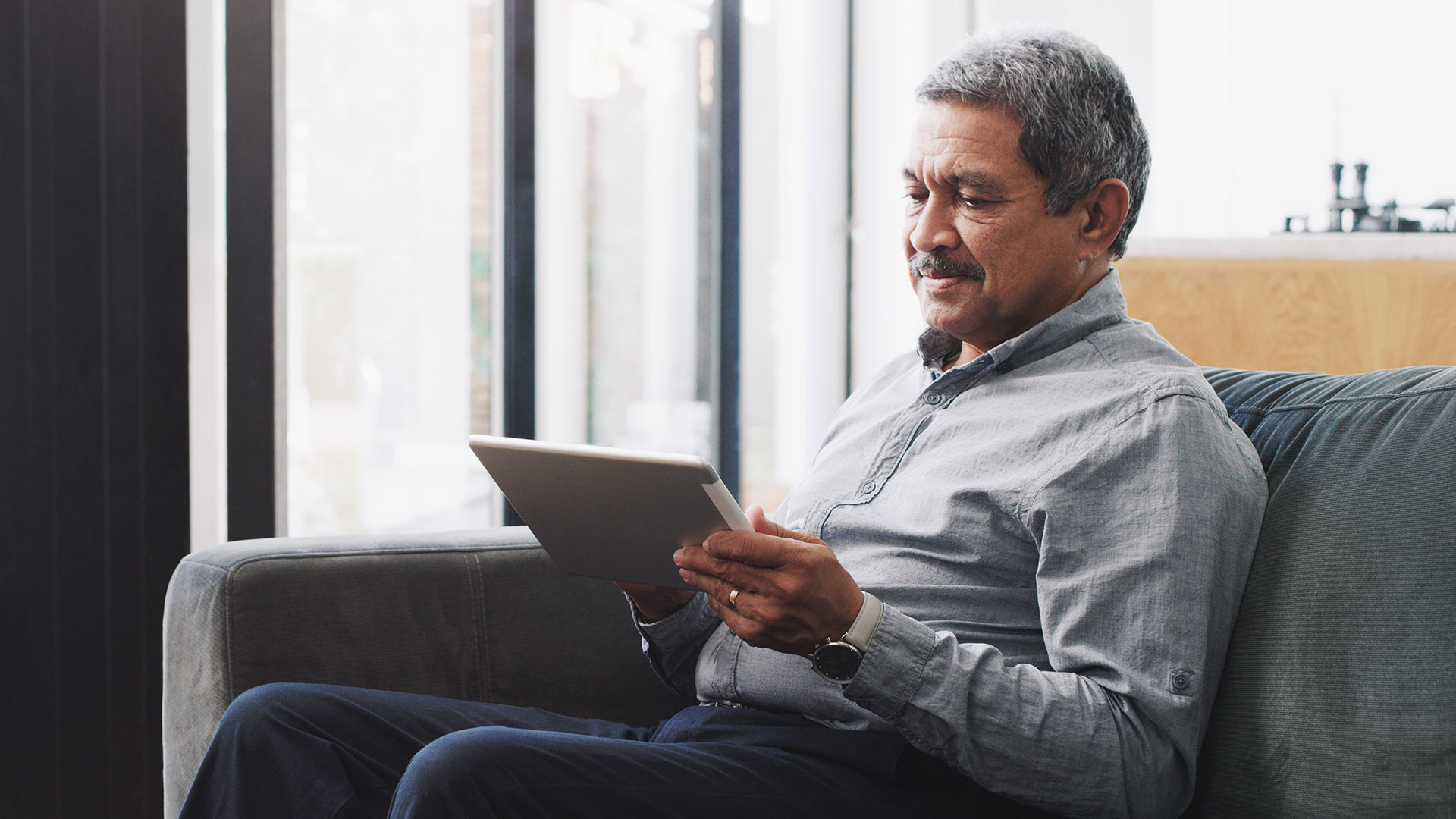 A person sits on a couch and looks at a tablet.