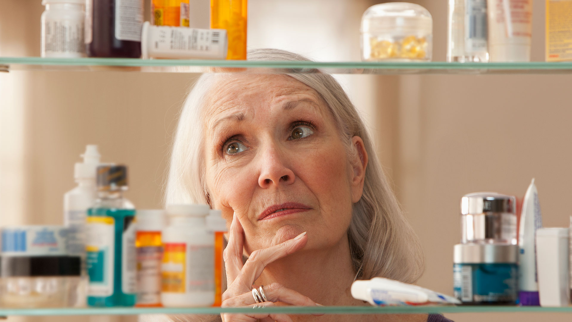 A person looks into a medicine cabinet that has prescription bottles and other toiletries.