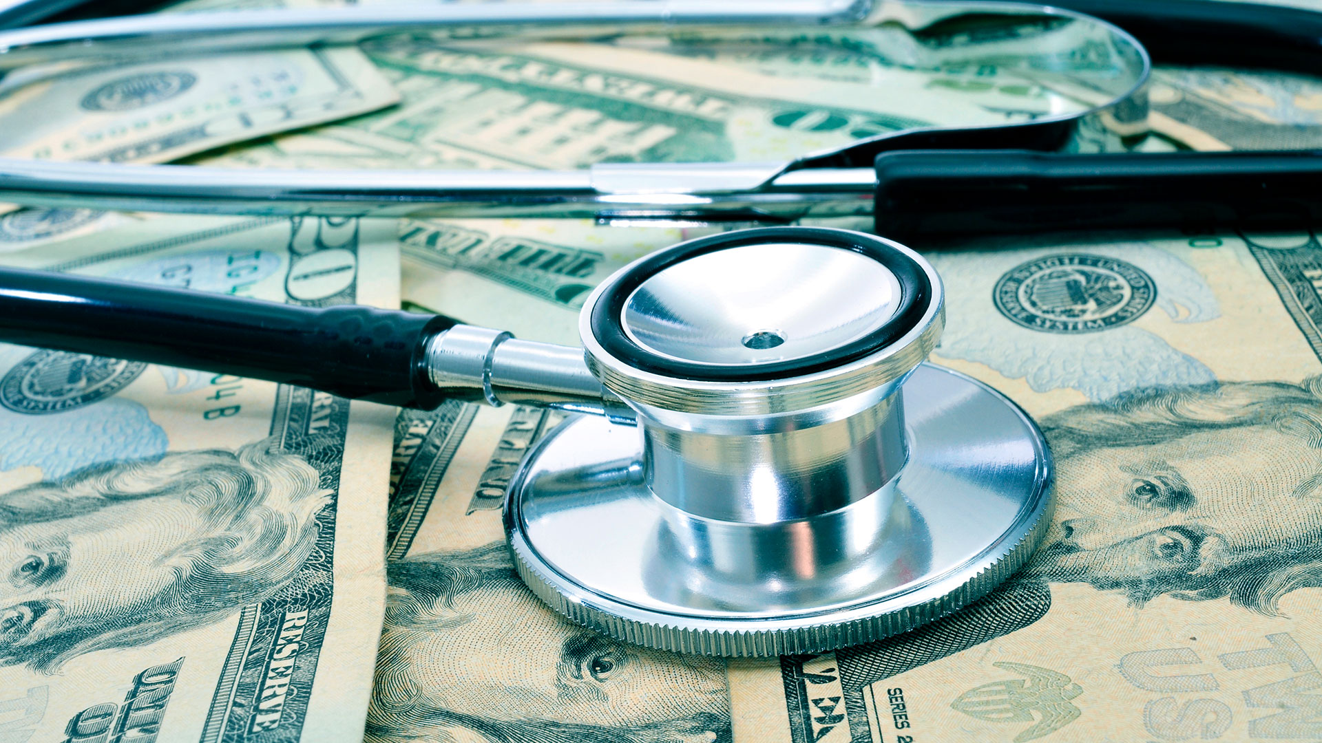 A stethoscope sits on several scattered twenty-dollar bills.