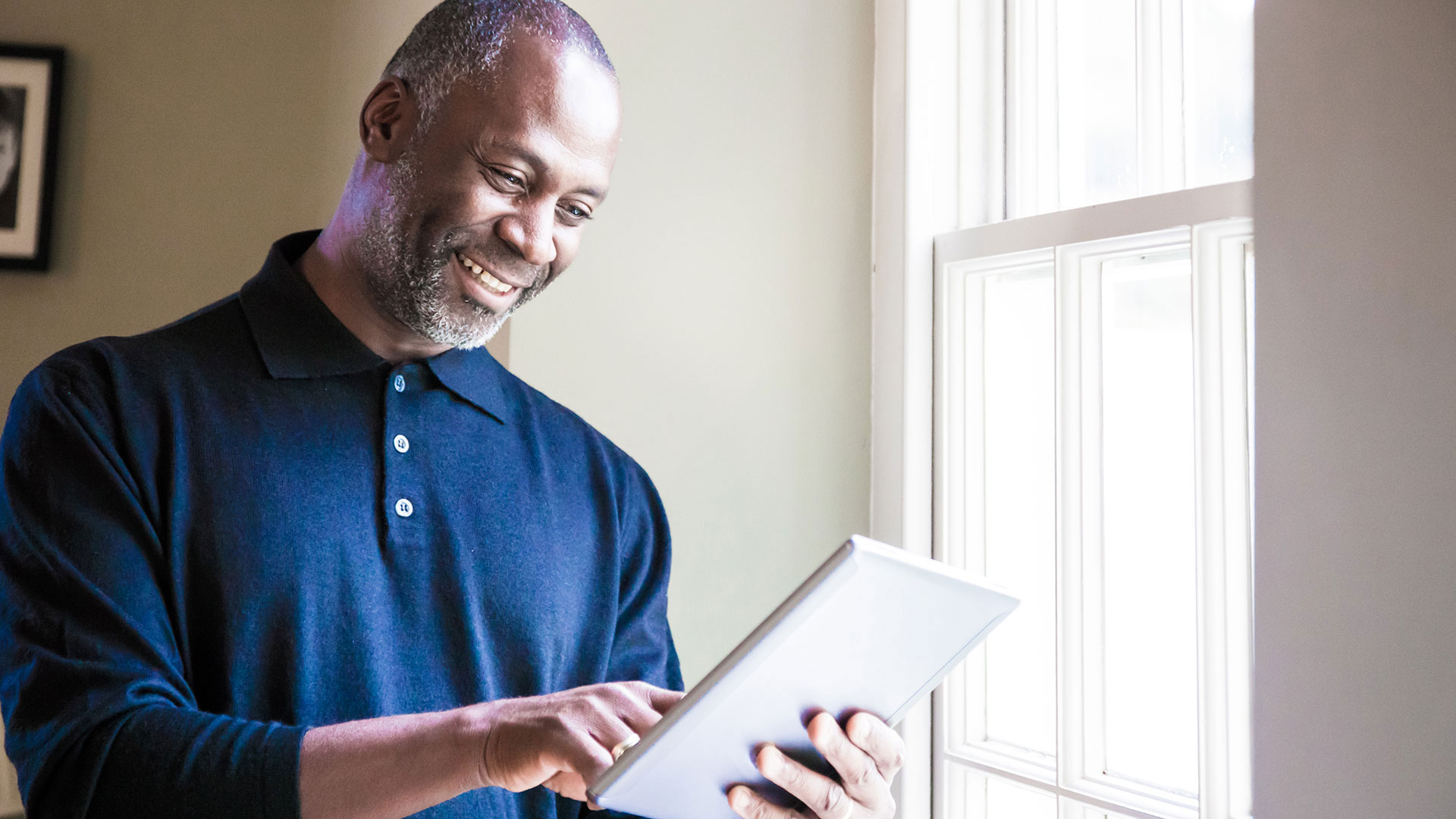 A person stands by a window and looks at a tablet.