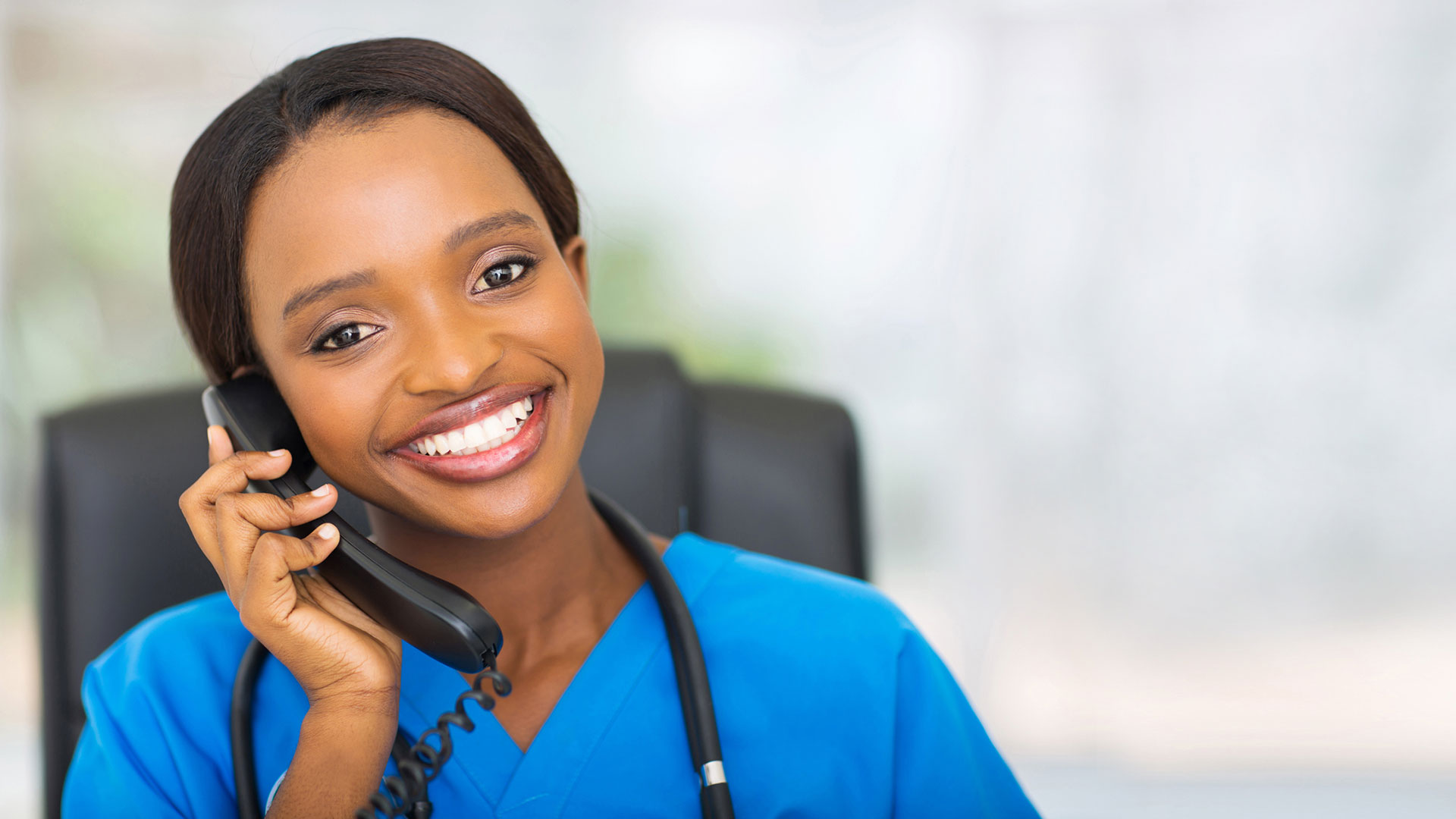 A nurse sits in a chair and talks on a phone.