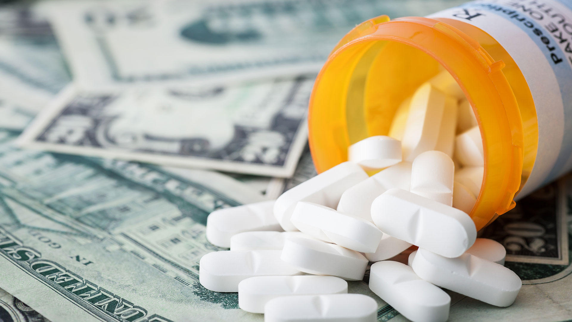 An open prescription bottle with pills spills on several scattered twenty-dollar bills.