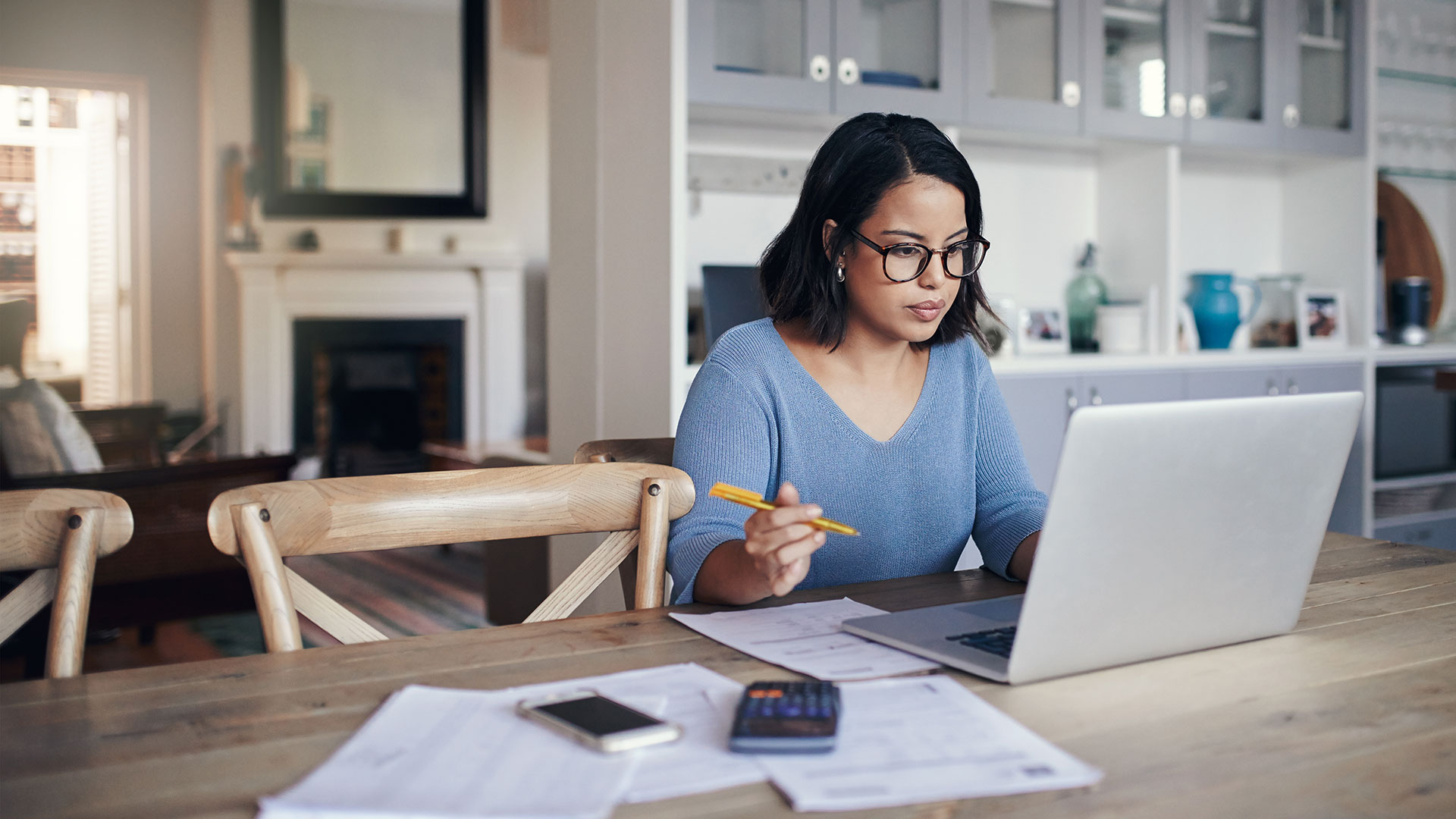 A person sits at a kitchen table and looks at a laptop.