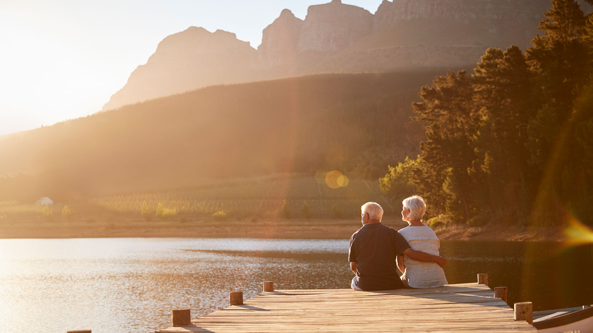 Two people sit on a dock and embrace.