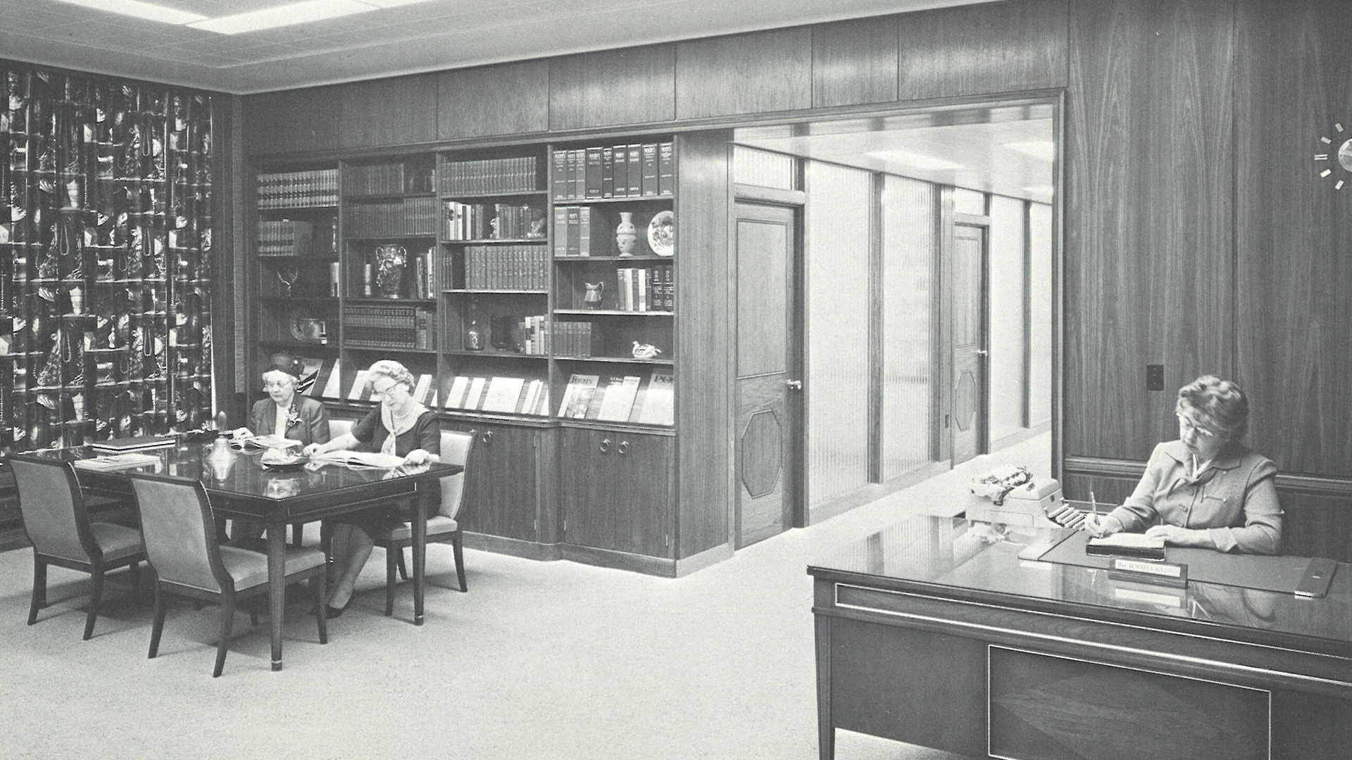 Two STRS Ohio members in 1962 sit at a table and read while an STRS Ohio associate sits at a desk and writes.