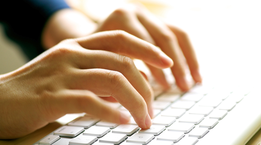 Photo of hands typing on a computer keyboard.